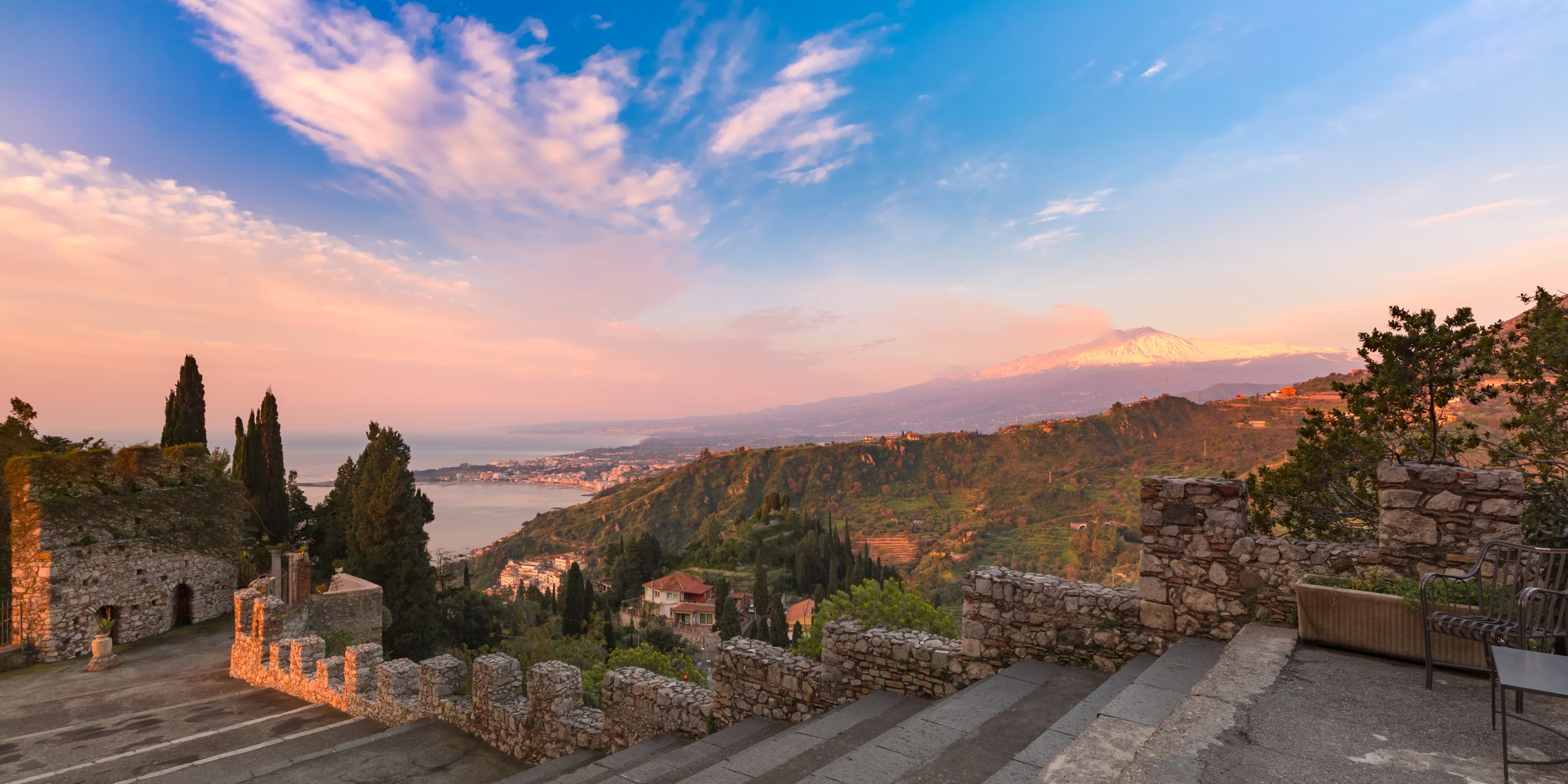 Panoramic view of smoking snow-capped Mount Etna volcano at sunrise, as seen from Taormina, Sicily